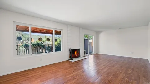 an empty room with wooden floor fireplace and windows