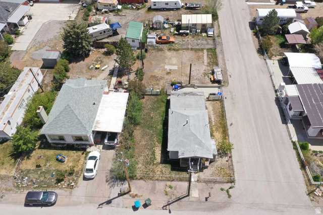 399 2nd E Street Helper, UT 84526 - Photo 11 of 19 Two distinct single-story residences with pitched shingle roofs and concrete driveways, accompanied by a spacious undeveloped lot
