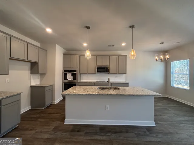 a large kitchen with kitchen island a stove a sink a refrigerator and white cabinets with wooden floor