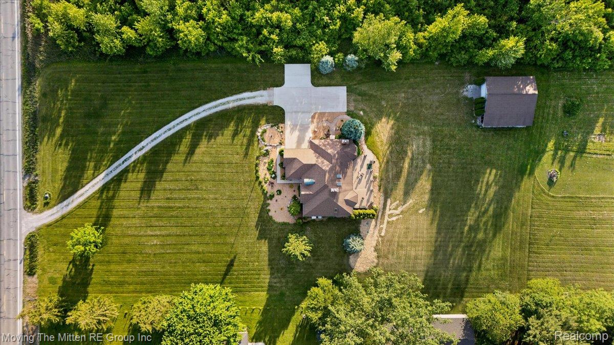 39750 Willow Road New Boston, MI 48164 - Photo 60 of 68 Aerial view showcasing a main residence with a distinct roofline, an expansive green lawn, mature trees bordering the property, a curved gravel driveway, and a detached auxiliary building