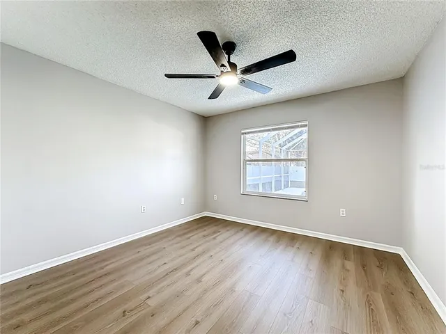 an empty room with wooden floor ceiling fan and windows
