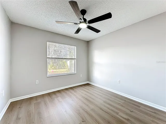 an empty room with wooden floor ceiling fan and windows