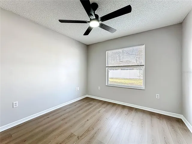 an empty room with wooden floor ceiling fan and windows