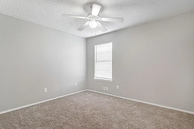 an empty room with a chandelier fan and windows