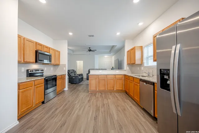 a large kitchen with stainless steel appliances granite countertop a refrigerator a stove top oven a sink dishwasher and wooden cabinets with wooden floor
