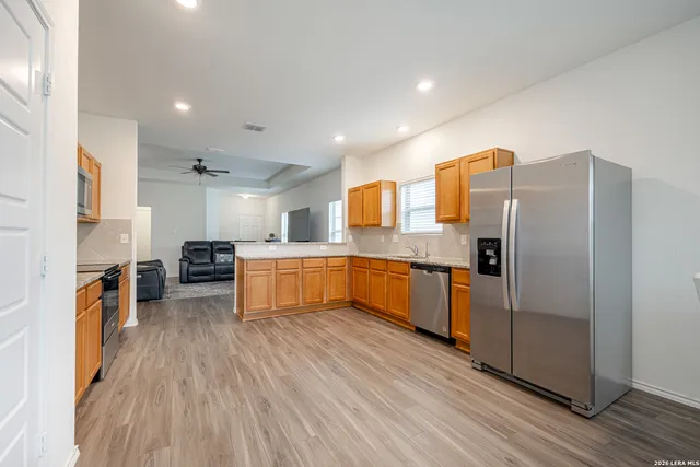 a large kitchen with stainless steel appliances granite countertop a refrigerator a sink dishwasher a stove and a dining table with wooden floor