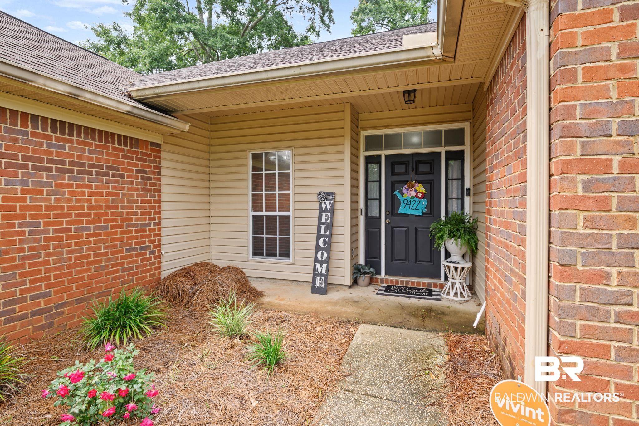 9422 Labrador Run South Mobile, AL 36695 - Photo 5 of 36 Entryway featuring a dark paneled door with sidelights, a transom window, and an overhead light fixture, complemented by tan siding and brick accents