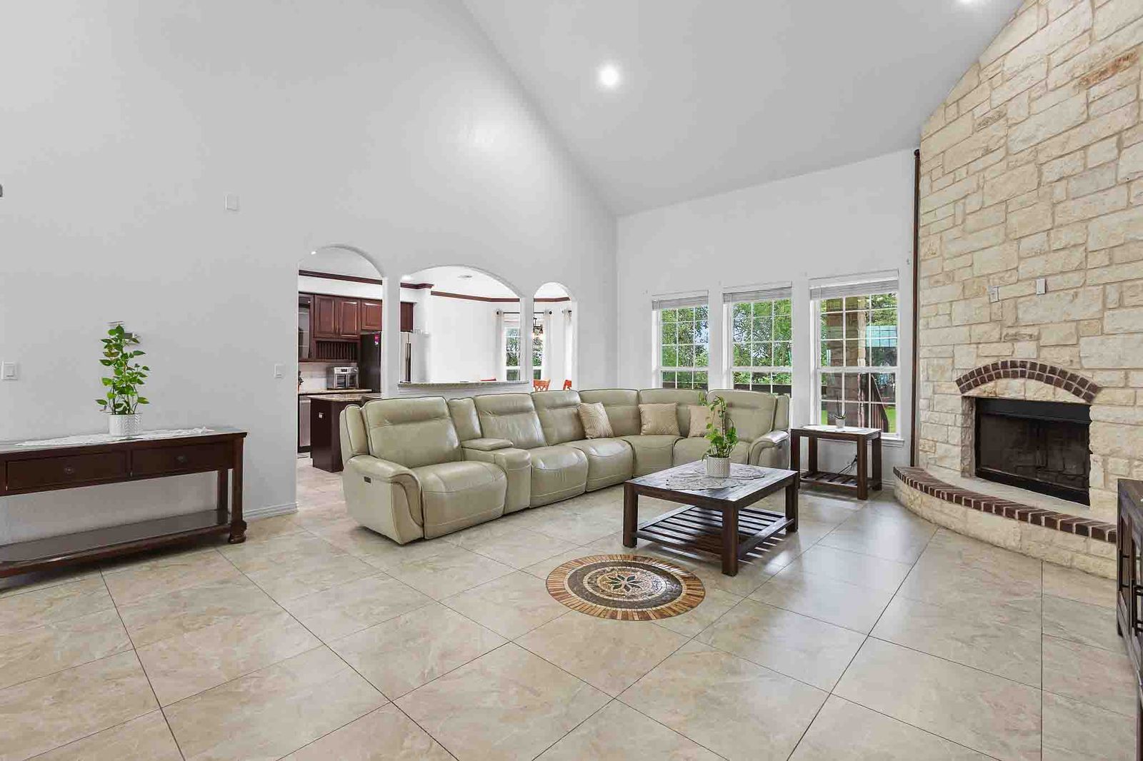 323 Woodbrook Trail Buda, TX 78610 - Photo 13 of 40 Vaulted ceiling living area featuring a stone fireplace with a brick hearth, large windows, and tile flooring with a decorative inlay