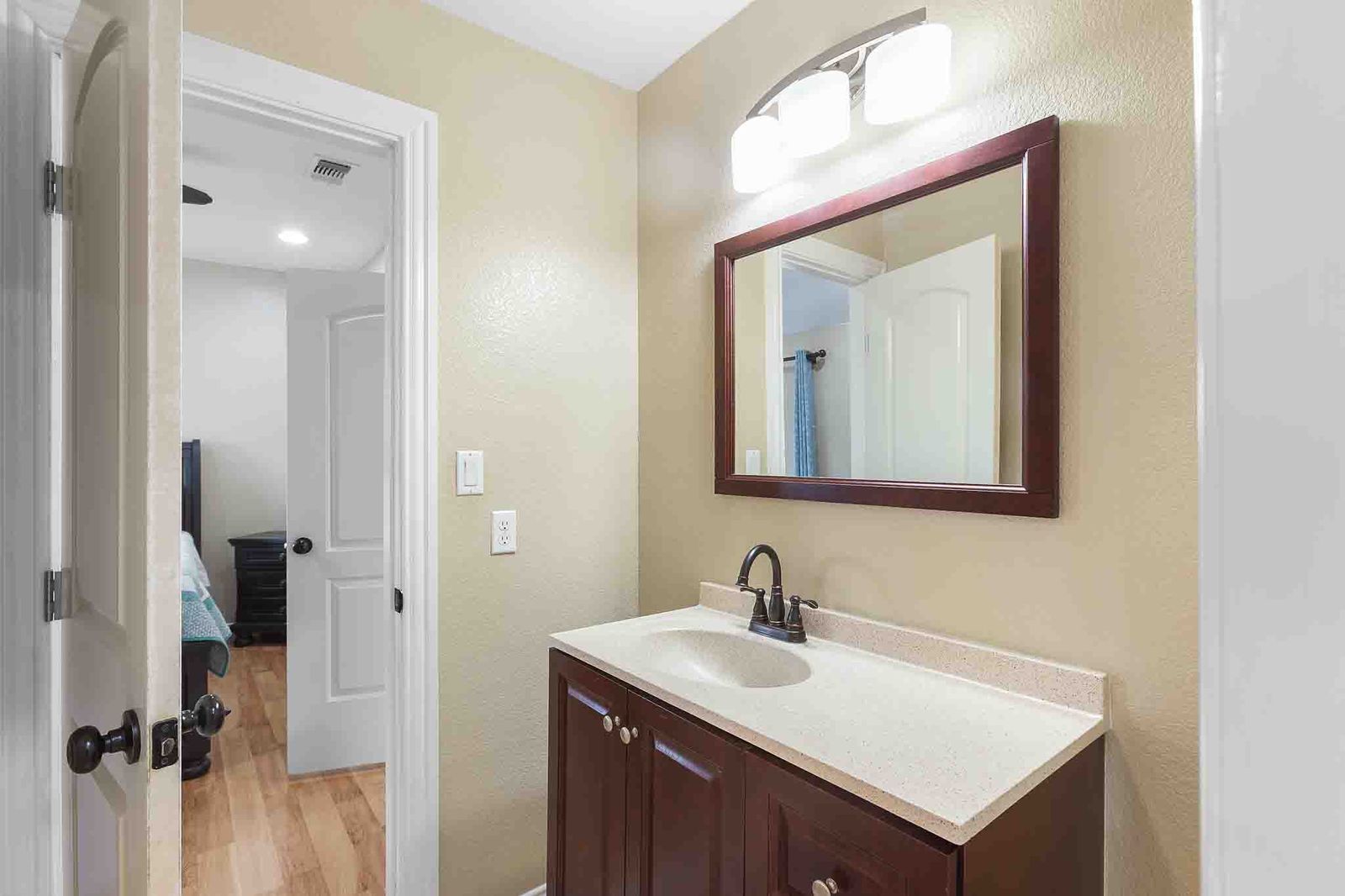323 Woodbrook Trail Buda, TX 78610 - Photo 24 of 40 Jack-n-Jill bathroom featuring a dark wood-finish cabinet with silver-tone hardware, a light-toned countertop with an integrated sink, a dark bronze-finish faucet, and a rectangular mirror with a dark wood-finish frame