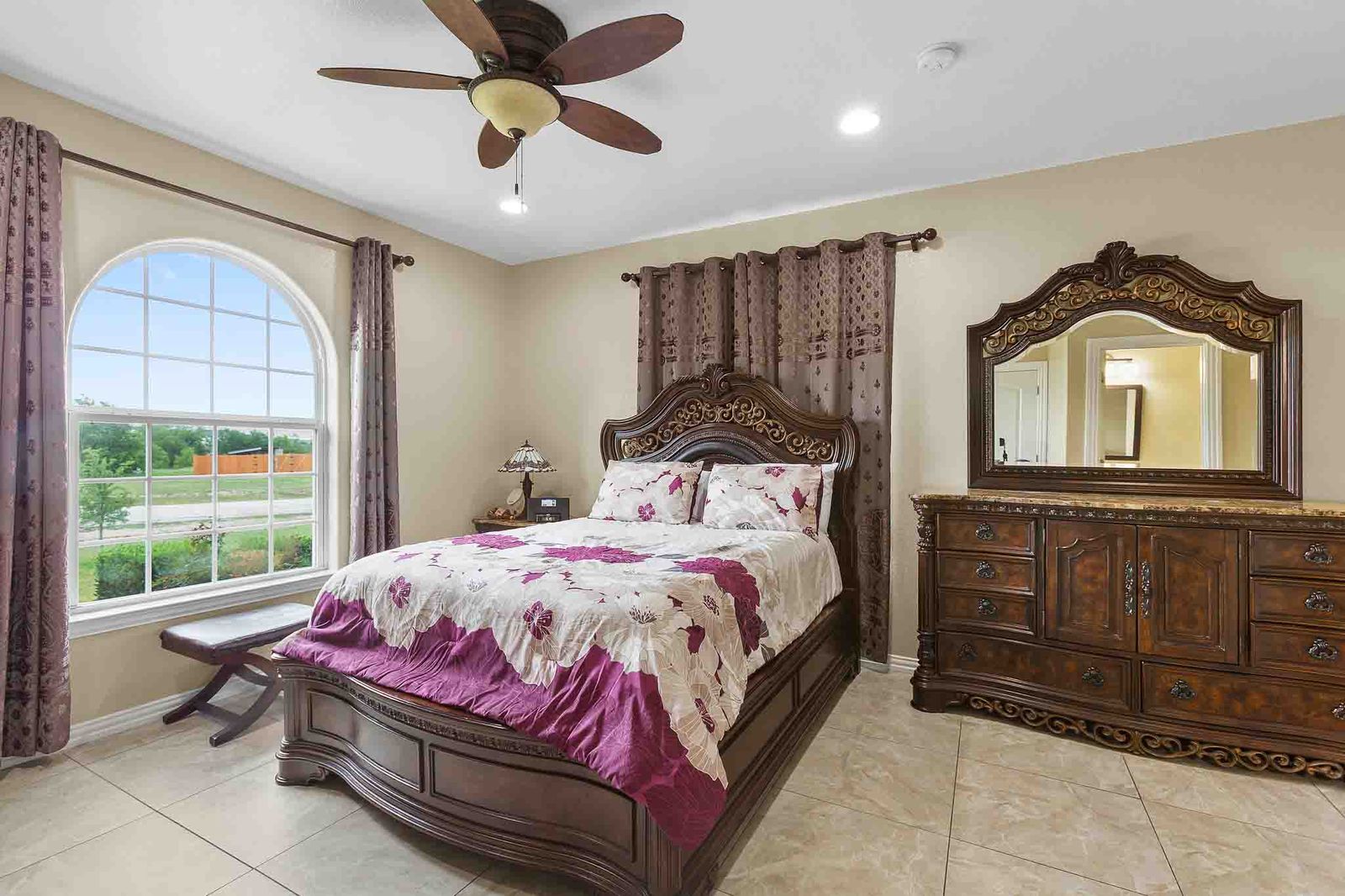 323 Woodbrook Trail Buda, TX 78610 - Photo 31 of 40 Spacious second primary bedroom featuring a large arched window with grid pattern, neutral-toned walls, and square tile flooring