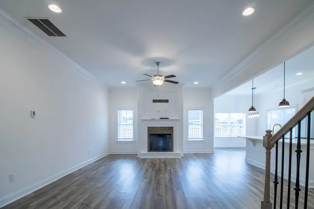 an empty room with wooden floor fireplace and a kitchen view
