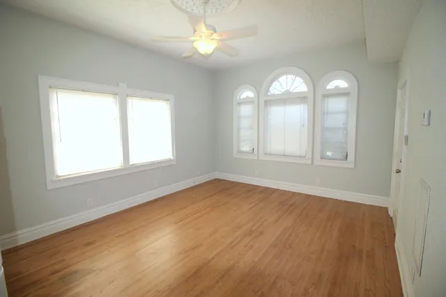 an empty room with wooden floor windows and fan