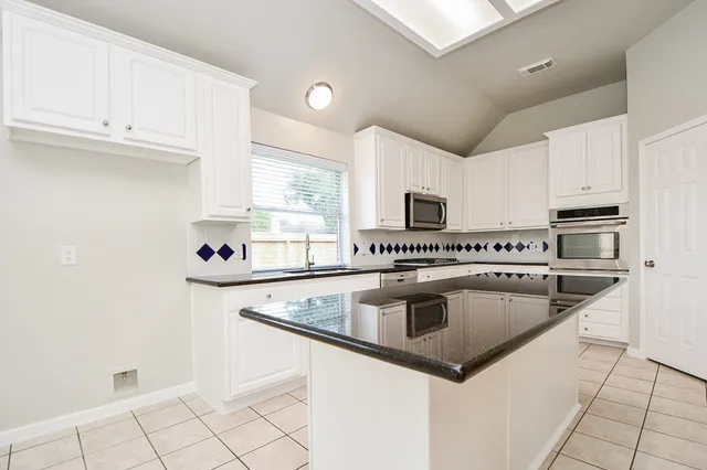 a kitchen with granite countertop a sink dishwasher stove and white cabinets