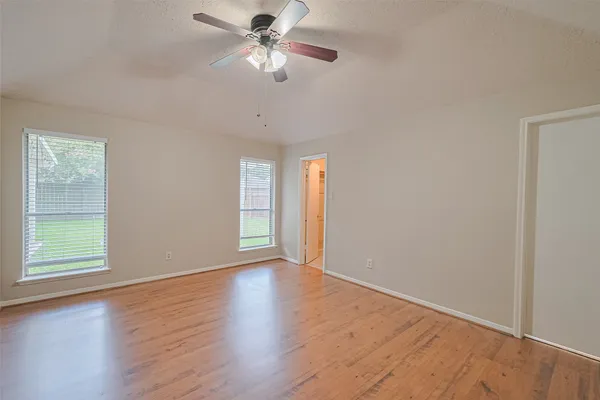 an empty room with wooden floor chandelier fan and windows