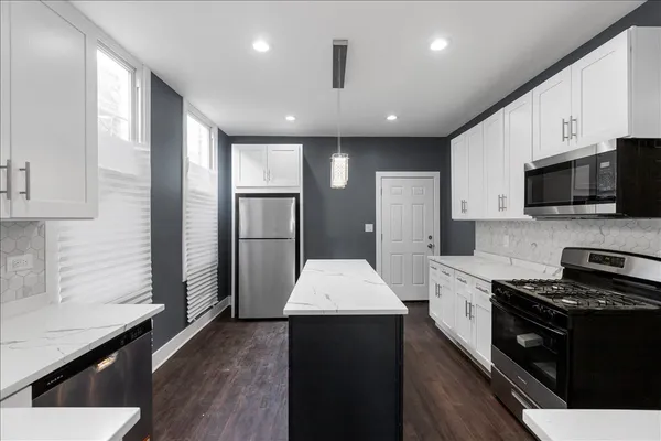 a large kitchen with stainless steel appliances kitchen island granite countertop a refrigerator a sink dishwasher a stove and white cabinets with wooden floor