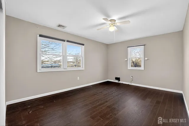 a view of an empty room with wooden floor and a ceiling fan