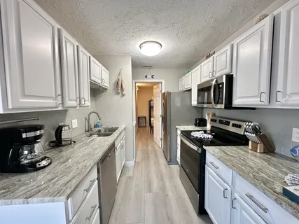 a kitchen with stainless steel appliances granite countertop a stove top oven a sink a refrigerator white cabinets and wooden floor