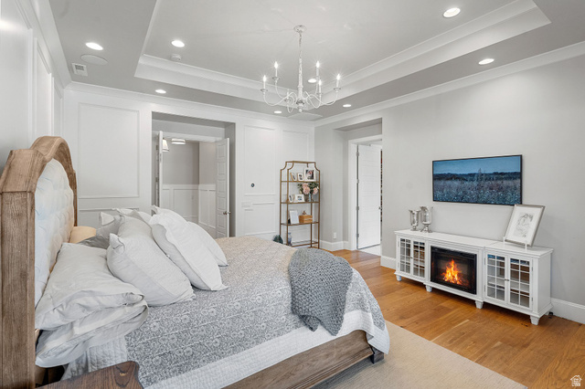 2917 Old Farm Road Washington, UT 84780 - Photo 41 of 105 Bedroom with hanging lights, a tray ceiling, light wood-type flooring, ornamental molding, and a glass covered fireplace