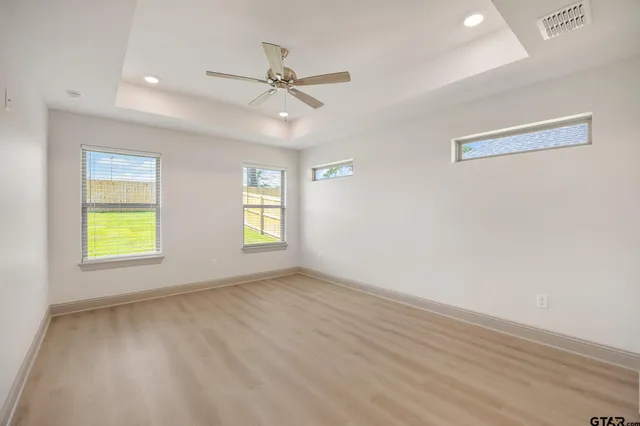 an empty room with ceiling fan and windows
