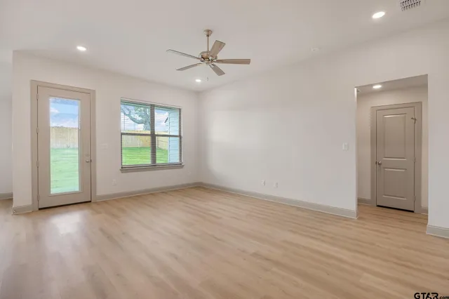 an empty room with wooden floor ceiling fan and windows
