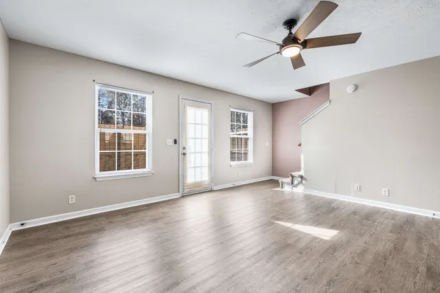 an empty room with wooden floor fan and windows
