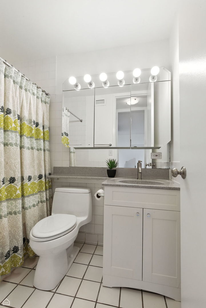 720 West Gordon Terrace, Unit 16E Chicago, IL 60613 - Photo 14 of 34 a bathroom with a toilet a sink a mirror a shower a window and vanity