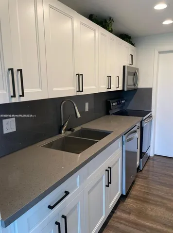 a kitchen with stainless steel appliances a sink dishwasher and white cabinets with wooden floor