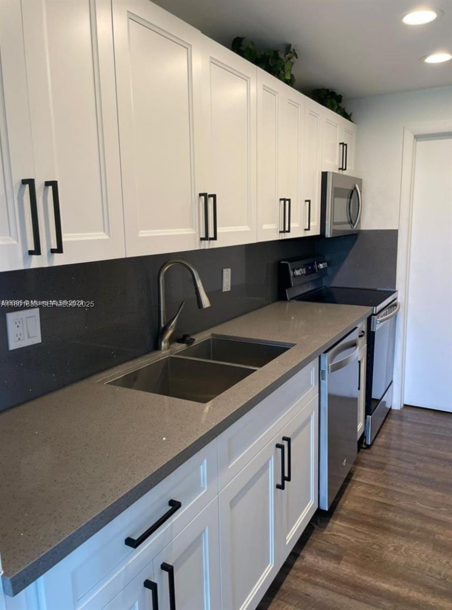 a kitchen with stainless steel appliances a sink dishwasher and white cabinets with wooden floor