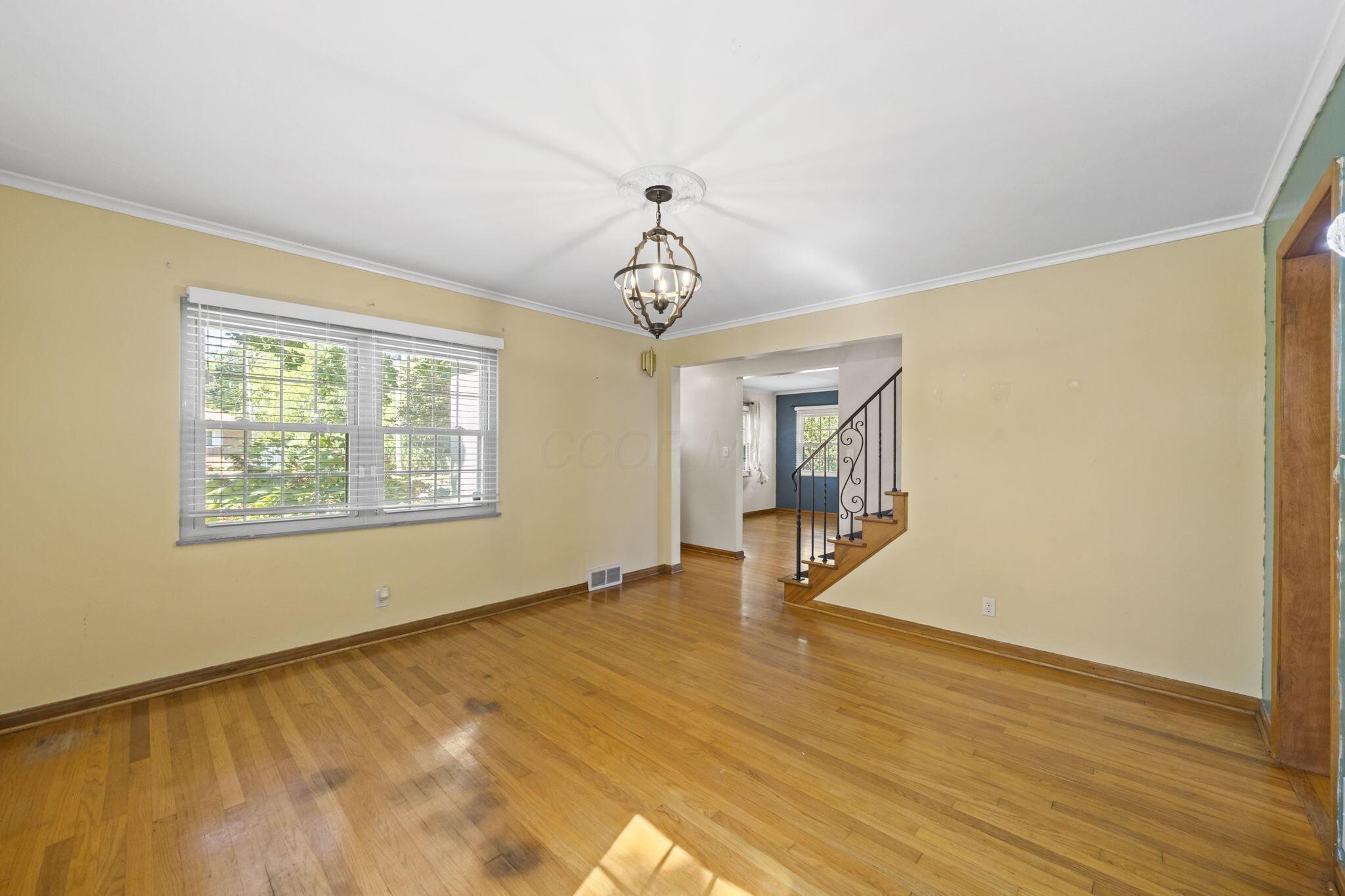40 South Kellner Road Columbus, OH 43209 - Photo 15 of 57 Hardwood flooring throughout, featuring a chandelier with ceiling medallion, a window with blinds, and a staircase with wrought iron railing