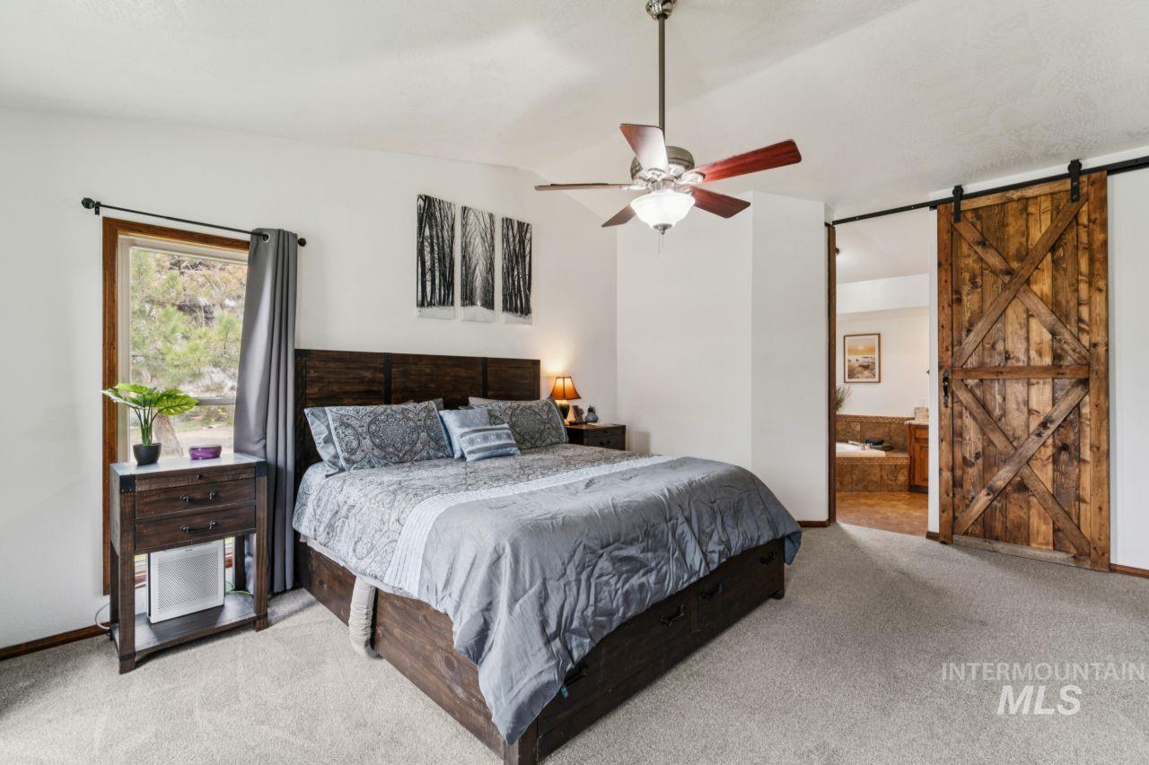 710 Keogh Lane Caldwell, ID 83607 - Photo 24 of 50 Bedroom featuring a barn door, lofted ceiling, ensuite bathroom, light colored carpet, and a ceiling fan