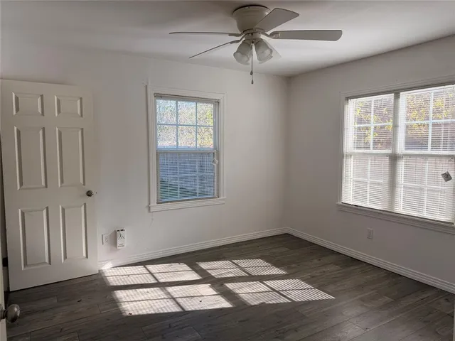 an empty room with wooden floor fan and windows