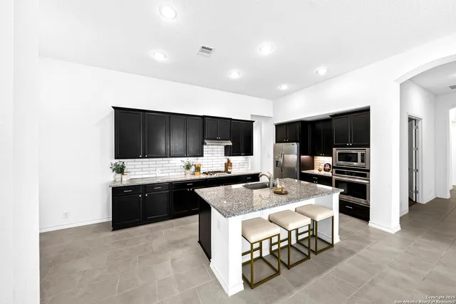 a kitchen with stainless steel appliances a stove top oven a sink dishwasher and a refrigerator with wooden floor