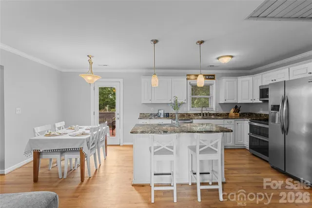a kitchen with stainless steel appliances kitchen island granite countertop a dining table chairs and white cabinets