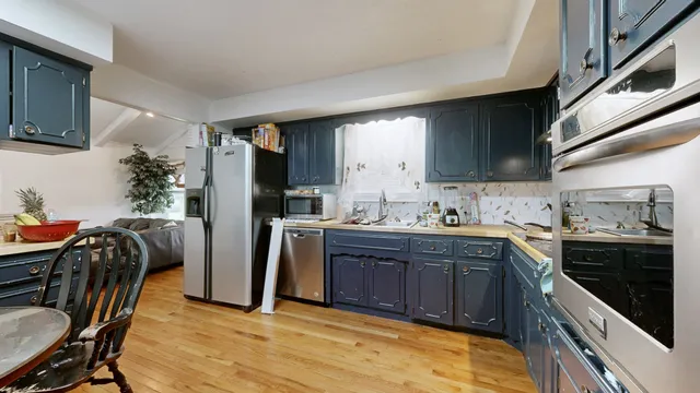 a kitchen with stainless steel appliances granite countertop a refrigerator a sink dishwasher a stove a dining table and chairs with wooden floor