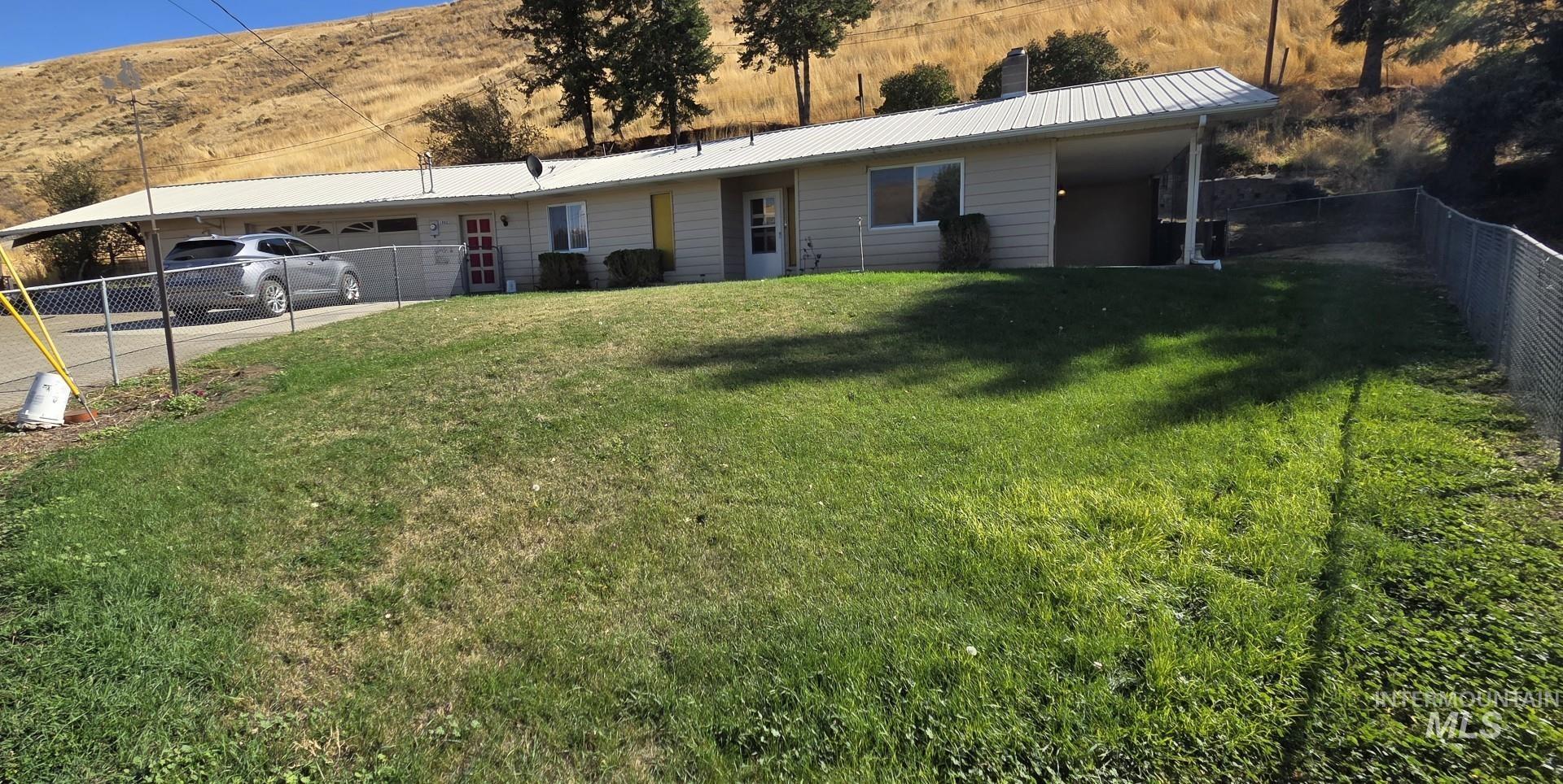 View of front of home with a metal roof, a fenced backyard, a garage, and driveway