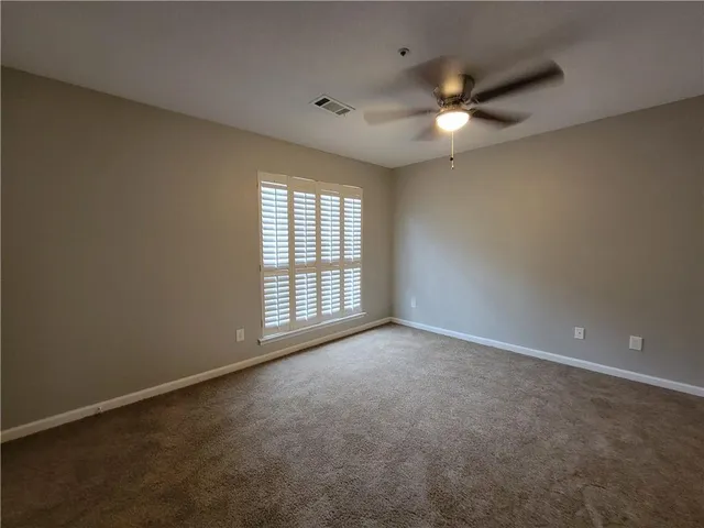 an empty room with chandelier fan and windows