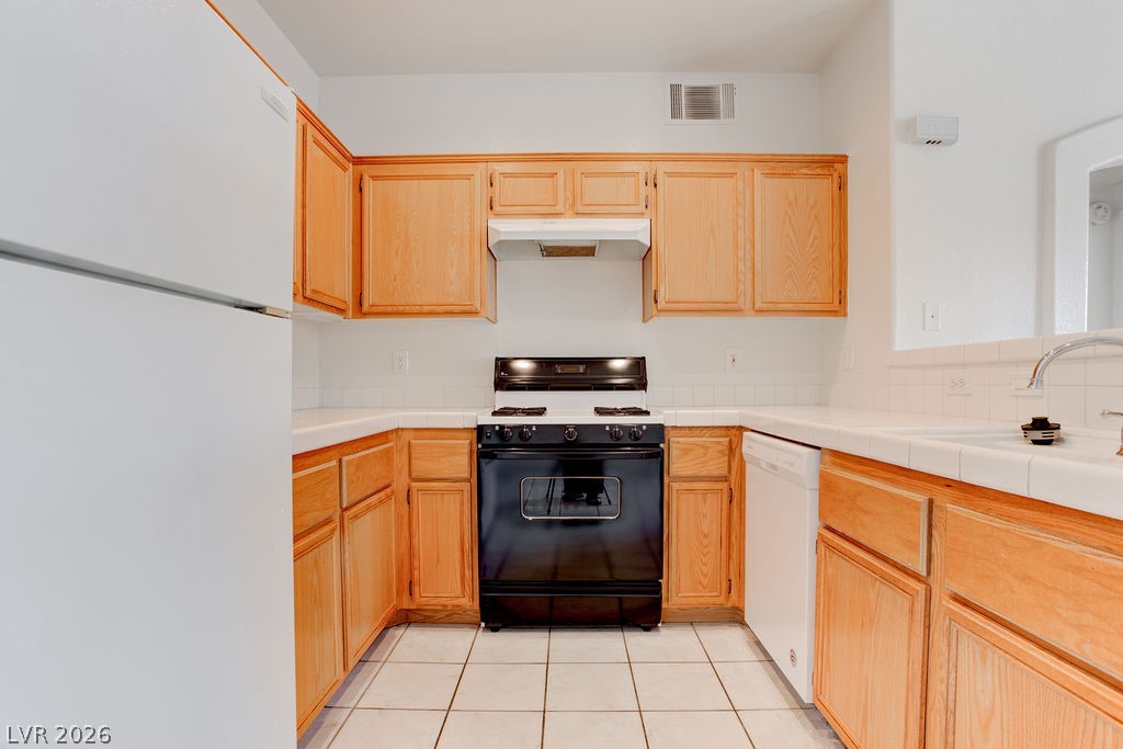 2201 Ramsgate Drive, Unit 326 Henderson, NV 89074 - Photo 23 of 44 Kitchen with white appliances, light wood finish cabinetry, and tile countertops