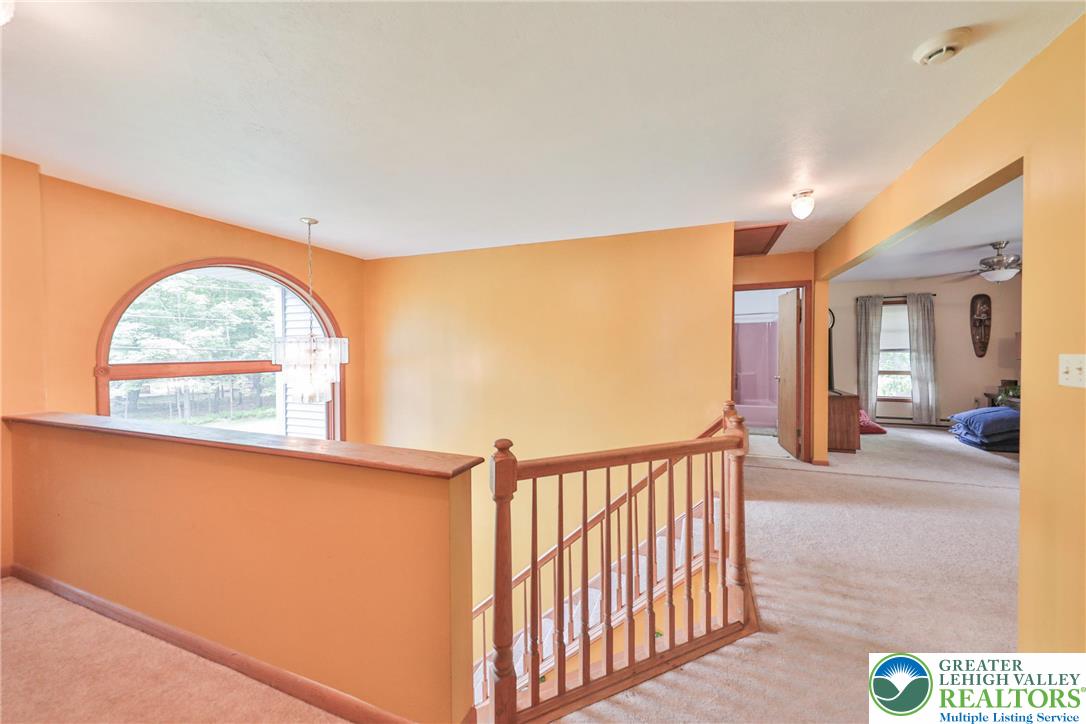 4608 Pine Ridge Drive West Bushkill, PA 18324 - Photo 34 of 62 An arched window and chandelier illuminate this upper-level hallway, boasting warm orange walls and a carpeted floor.