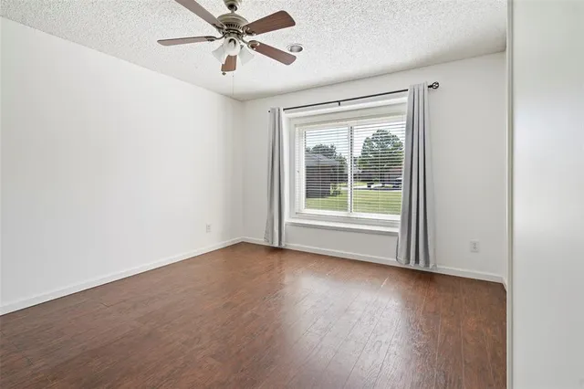 an empty room with wooden floor fan and windows