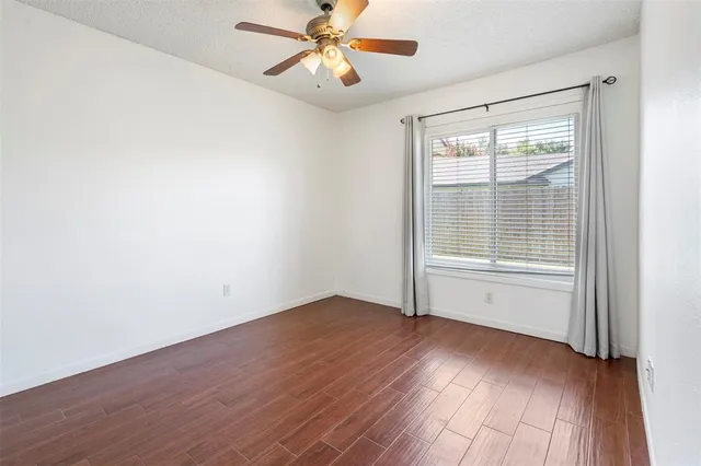 an empty room with wooden floor fan and windows
