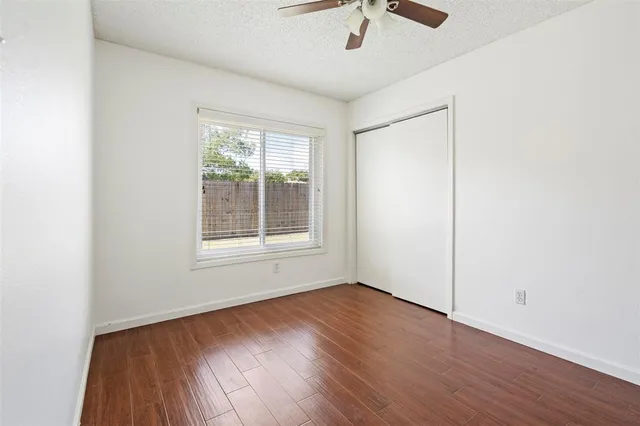 an empty room with wooden floor chandelier fan and windows
