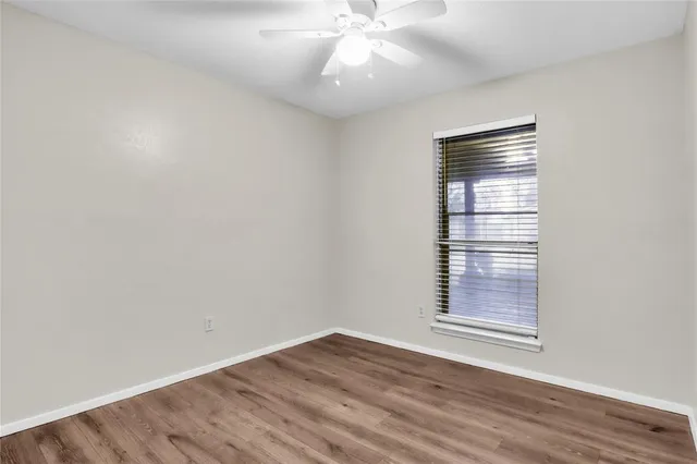 an empty room with wooden floor fan and windows