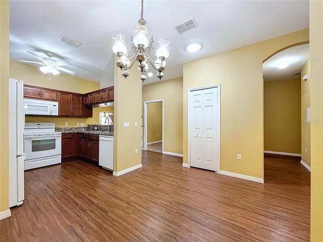 a view of an empty room and kitchen with wooden floor