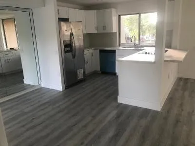 a kitchen with stainless steel appliances granite countertop a refrigerator a sink a stove and white cabinets with wooden floor