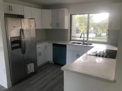 a kitchen with stainless steel appliances granite countertop a refrigerator a sink a stove and white cabinets with wooden floor