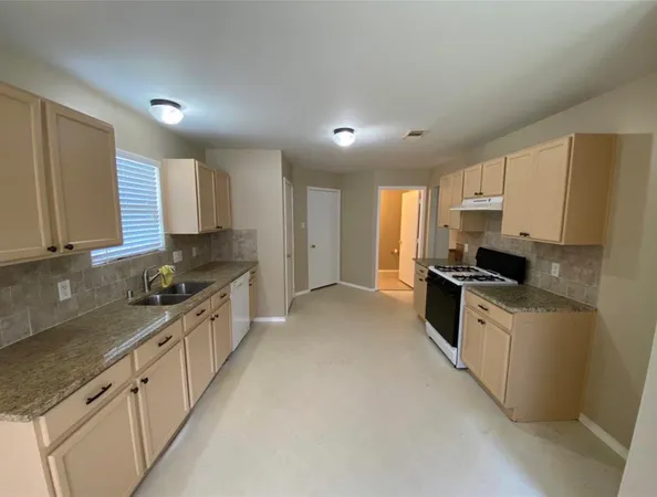 a kitchen with granite countertop a sink a stove refrigerator and cabinets