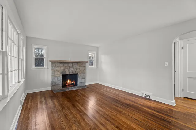 a view of an empty room with wooden floor fireplace and a window