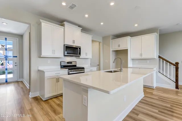 a large kitchen with stainless steel appliances granite countertop a stove a sink a refrigerator and white cabinets with wooden floor