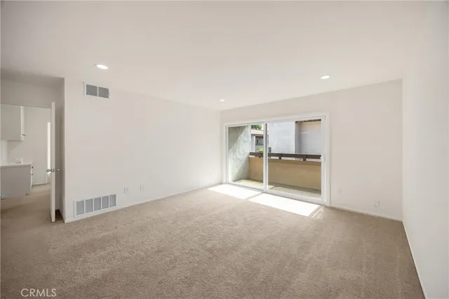 a view of an empty room with kitchen and window