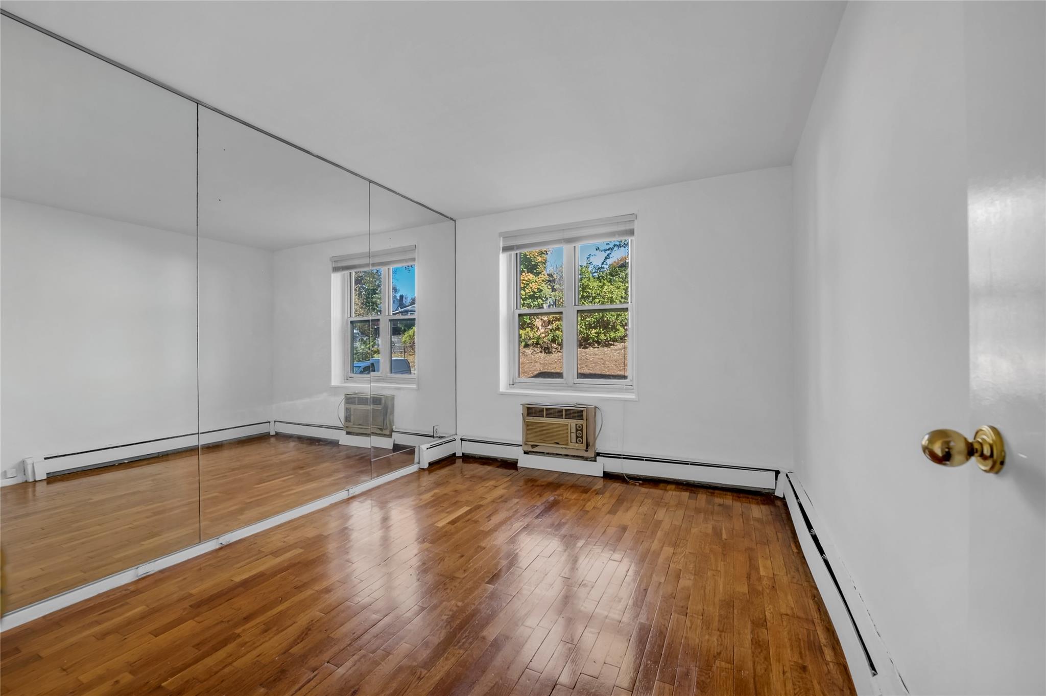 185 South Middle Neck Road, Unit 1G Great Neck, NY 11021 - Photo 6 of 9 Unfurnished room with a wall mounted AC, hardwood / wood-style floors, and a baseboard heating unit